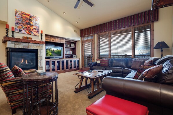 A cozy living room with a fireplace, leather furniture, and a large window with blinds. - EL5302 | Great Mountain Escape | Top Floor with Vaulted Ceiling | Air Chilling (Steamboat Springs)