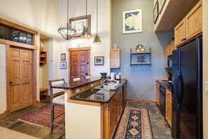 Una cocina con armarios de madera, un refrigerador negro, una encimera de granito y una lámpara colgante.