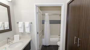 A bathroom with a sink, mirror, towel rack, shower curtain, bathtub, and toilet.