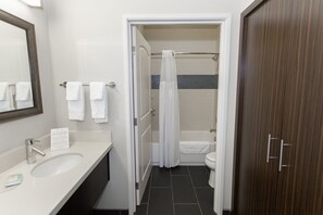 Ein Badezimmer mit Waschbecken, Spiegel, Handtuchhalter, Duschvorhang, Badewanne und Toilette.
