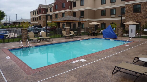A swimming pool with lounge chairs and umbrellas, surrounded by a building with stone and wood exterior.