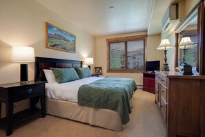 Une chambre d’hôtel comprenant un lit, des tables de chevet, une commode, un téléviseur et une fenêtre avec des stores.