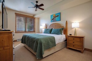 A bedroom with a bed, wooden headboard, two bedside lamps, a ceiling fan, a window with blinds, and a painting on the wall. - CL3209 | Newly Listed | Close to Skiing | Perfect for Couples | A/C (Steamboat Springs)
