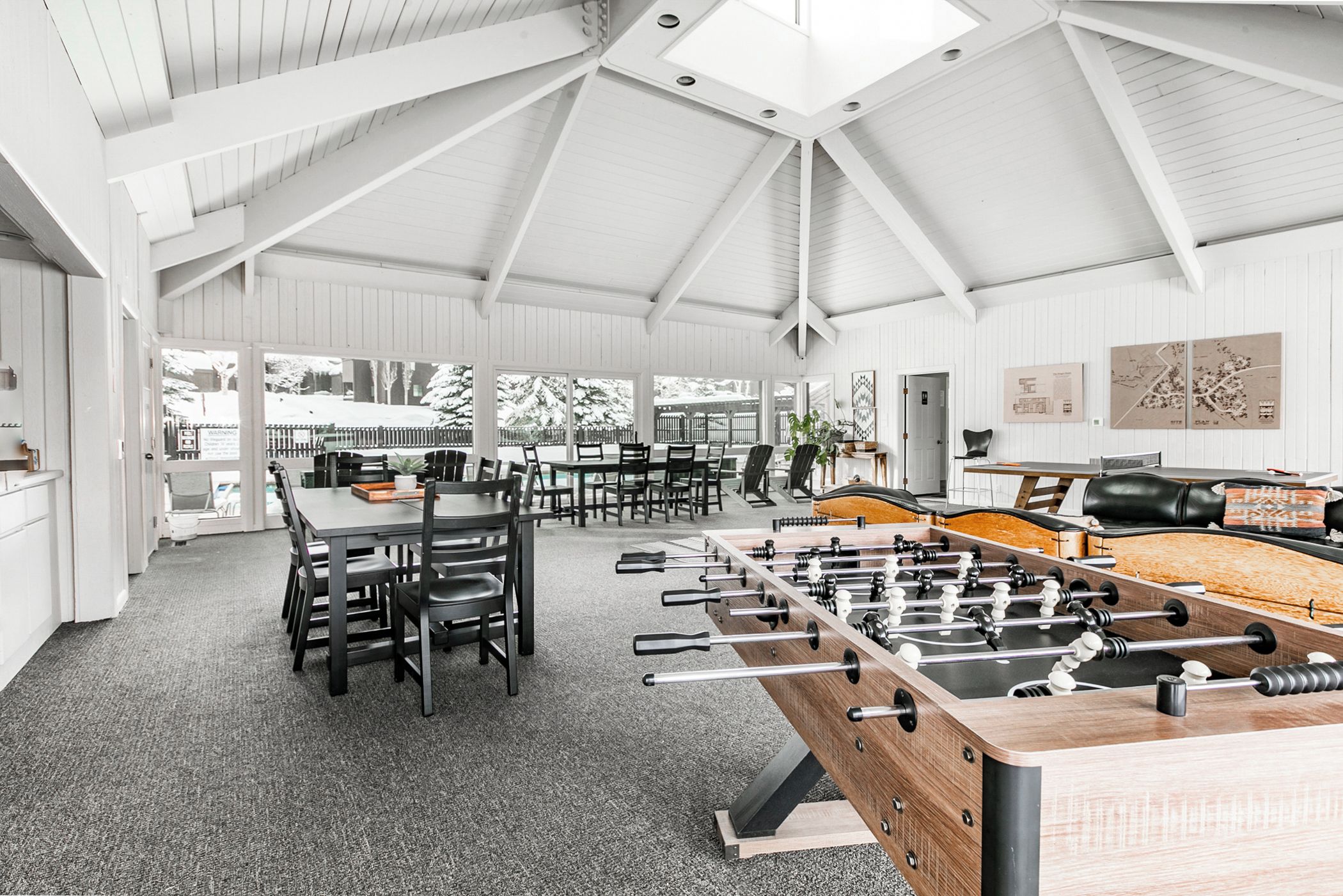 A spacious room with a high ceiling, a foosball table, and a dining area with chairs and tables.
