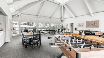 A spacious room with a high ceiling, a foosball table, and a dining area with chairs and tables.