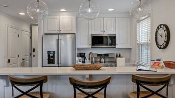 A modern kitchen with white cabinets, stainless steel appliances, a central island with bar stools, and pendant lighting.