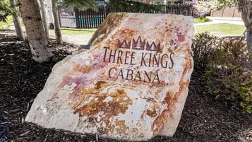 A weathered sign with the text 'THREE KINGS CABANA' in a rustic font, surrounded by mulch and trees.