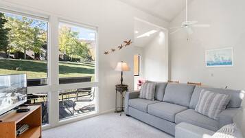 A modern living room with a grey sofa, a TV on a wooden stand, a floor lamp, and a ceiling fan.