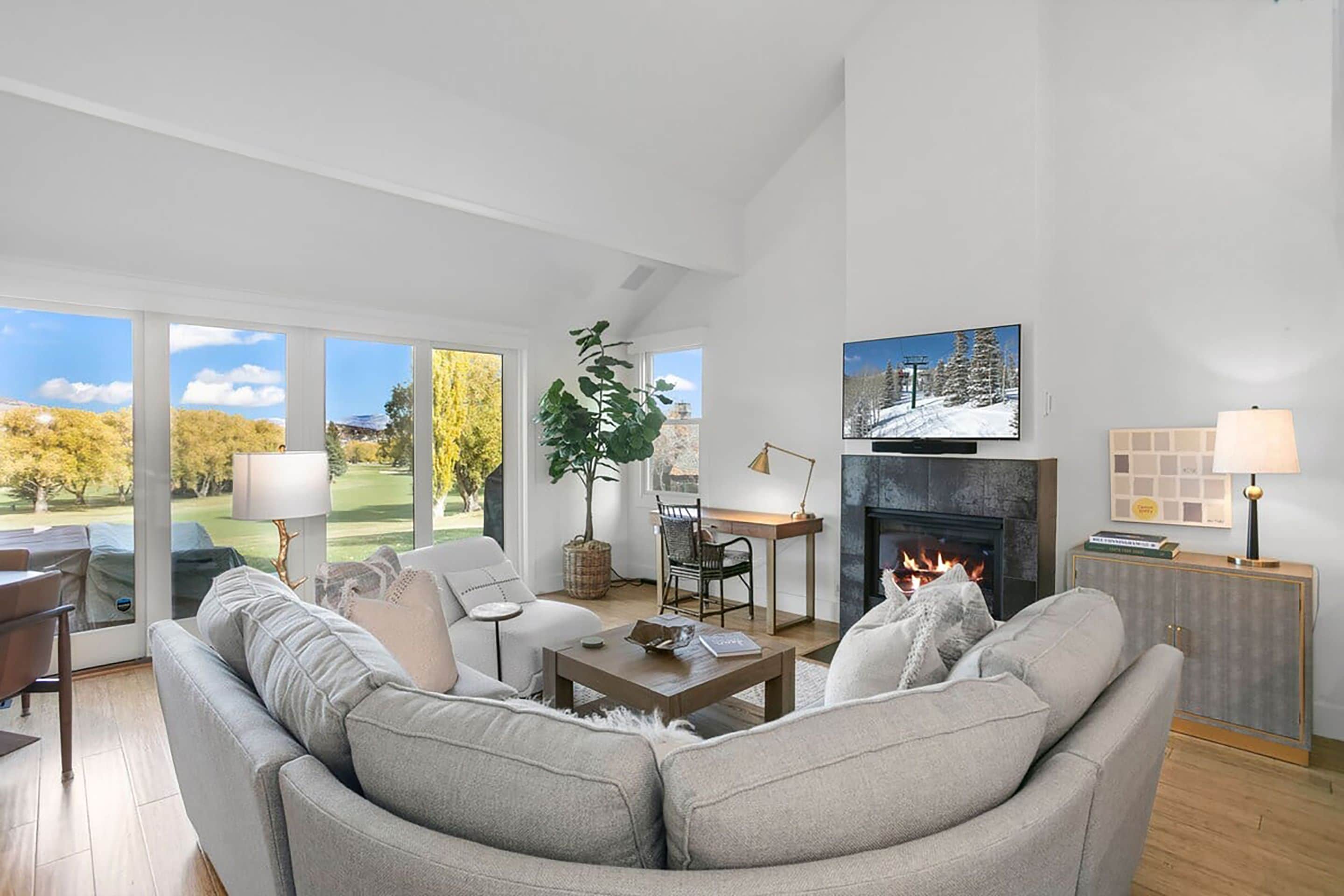 Een moderne woonkamer met een open haard, een televisie en uitzicht op een golfbaan.