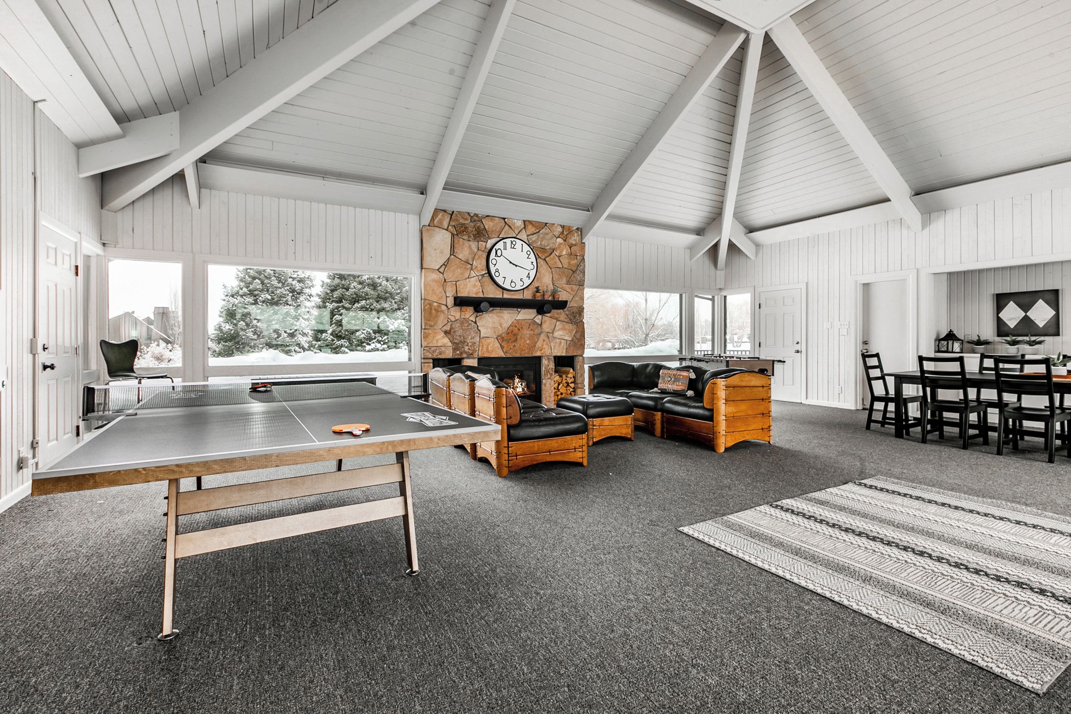 A spacious room with a ping pong table, a stone fireplace, leather seating, and a dining area with chairs and a table.