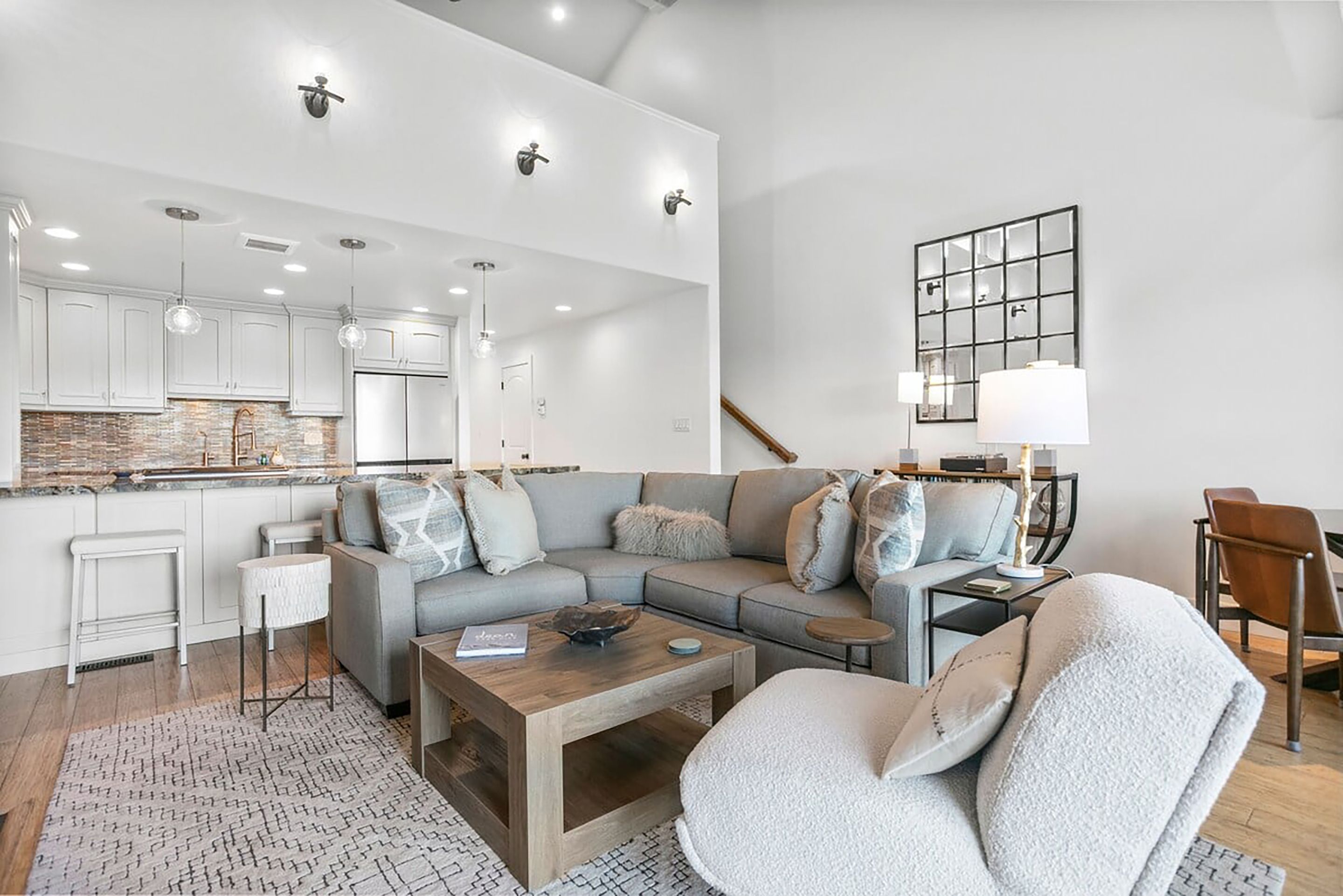 A modern living room with a sectional sofa, a coffee table, and a dining area with a kitchen in the background.