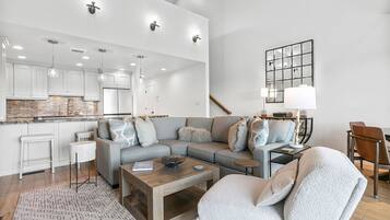 A modern living room with a sectional sofa, a coffee table, and a dining area with a kitchen in the background.