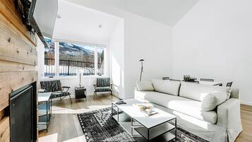Un salon moderne avec un canapé, une table basse et des fauteuils, de grandes fenêtres offrant une vue sur un paysage enneigé, et un mur en bois.