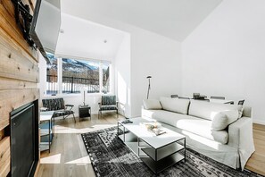Una sala de estar moderna con sofá, mesa de centro y sillones, ventanas amplias con vista a un paisaje nevado y una pared de madera.