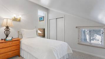 A bedroom with a bed, a nightstand, a lamp, a mirror, a wardrobe, and a window with blinds.