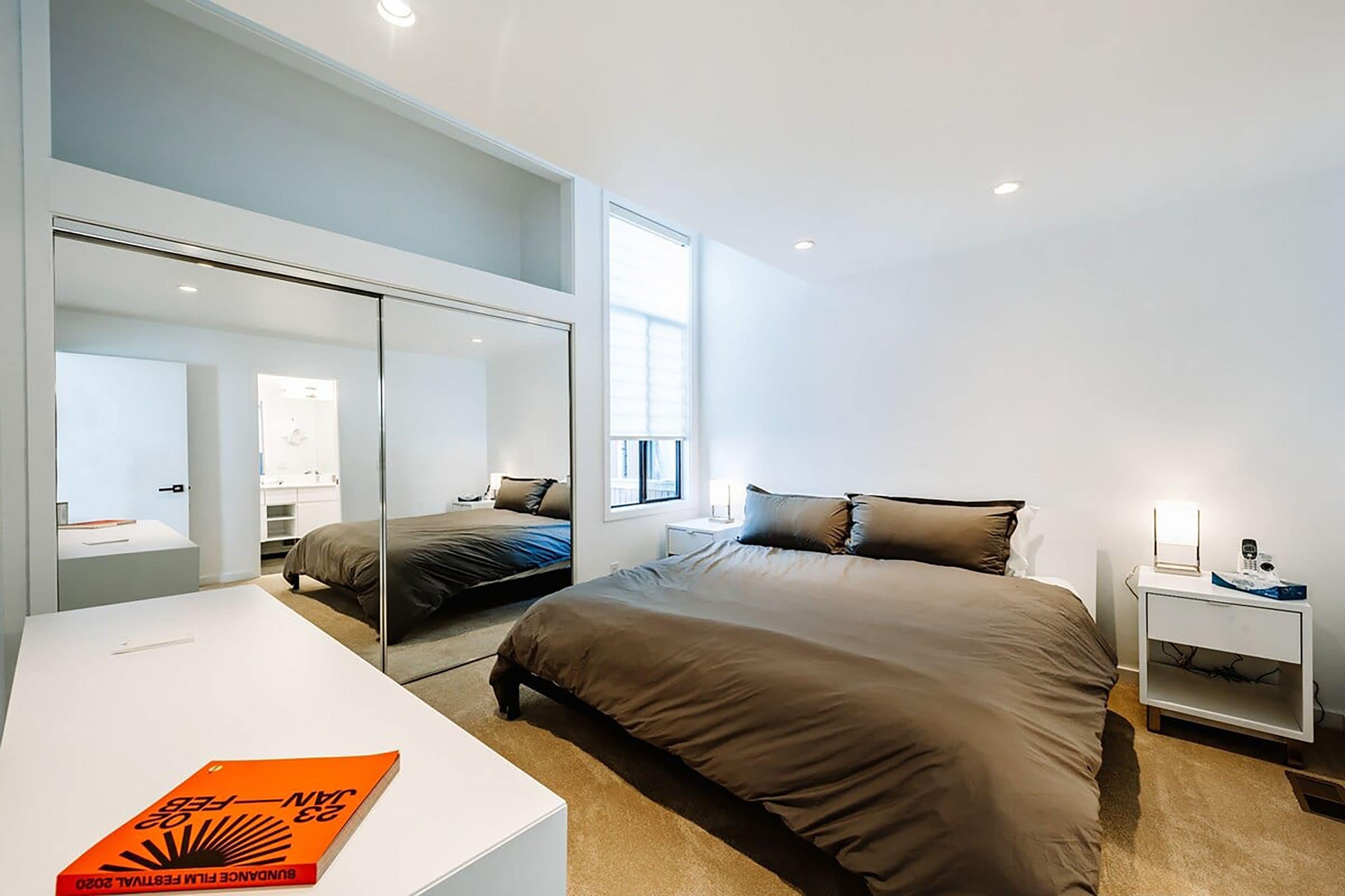 A modern bedroom with a large bed, a bedside table, a nightstand, and a mirror.