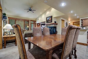 Une salle à manger avec une table en bois et des chaises à motifs, un ventilateur de plafond et une cheminée.