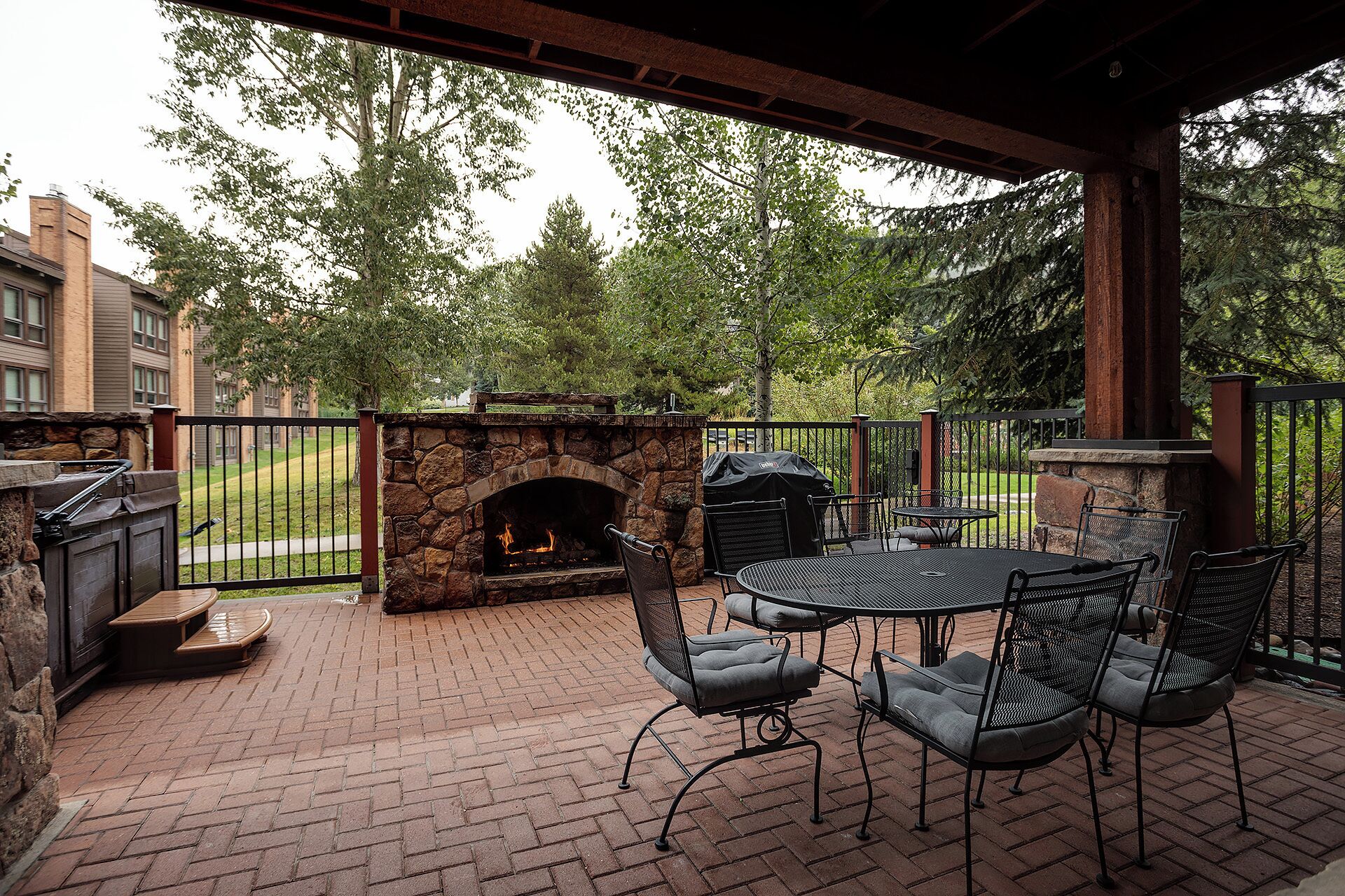 An outdoor patio with a stone fireplace, a grill, and a table with chairs.
