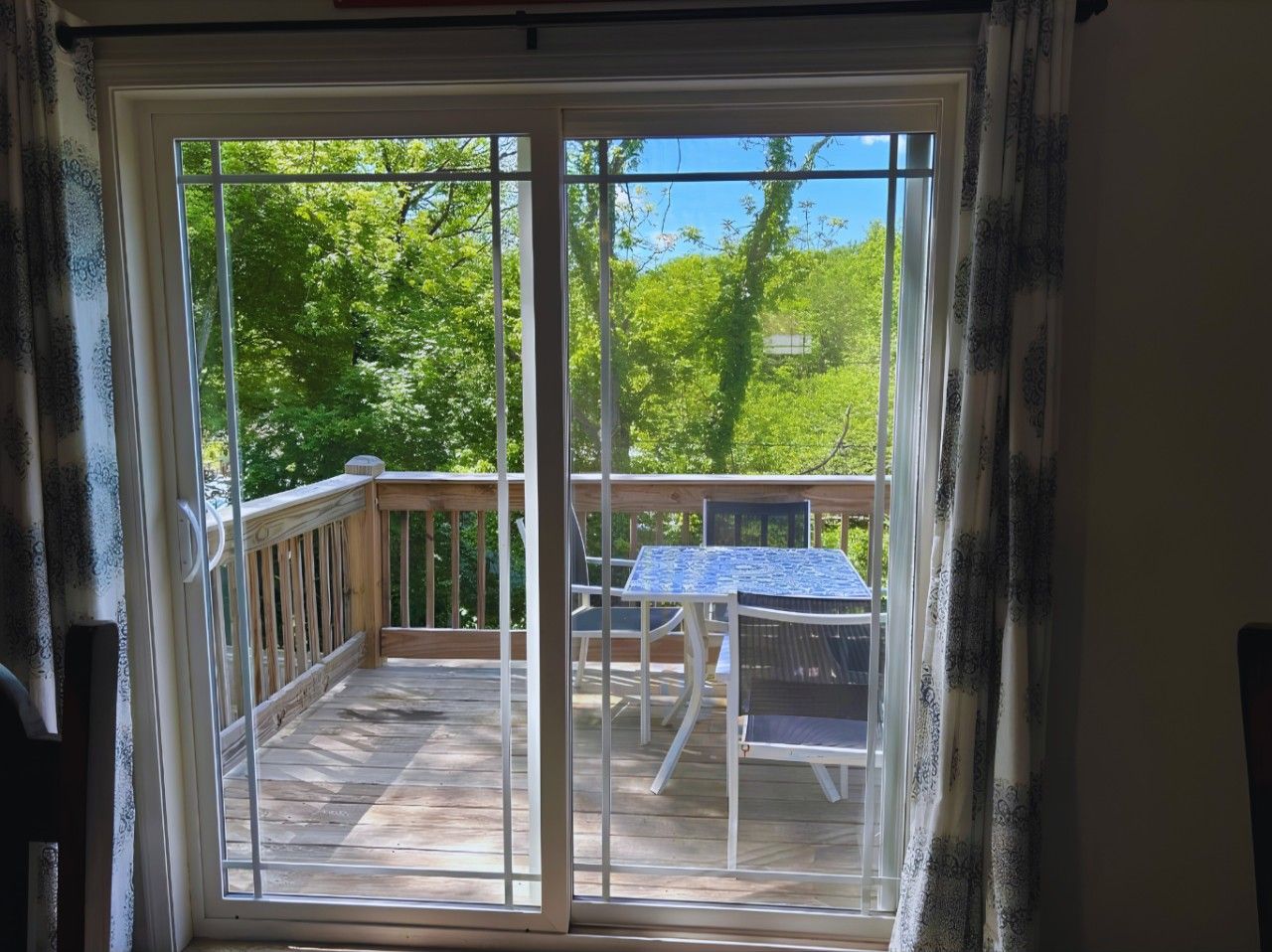 Blick durch eine Glastür auf eine Terrasse mit Tisch und Stühlen.