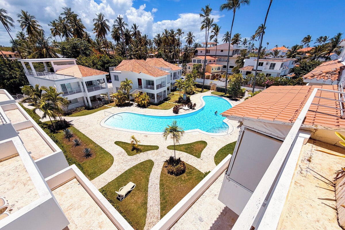 Um resort com piscina rodeada por palmeiras e edifícios com telhados vermelhos.