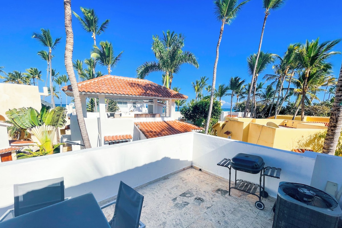 Terraço no telhado com mesa, cadeiras, churrasqueira e unidade de ar condicionado.