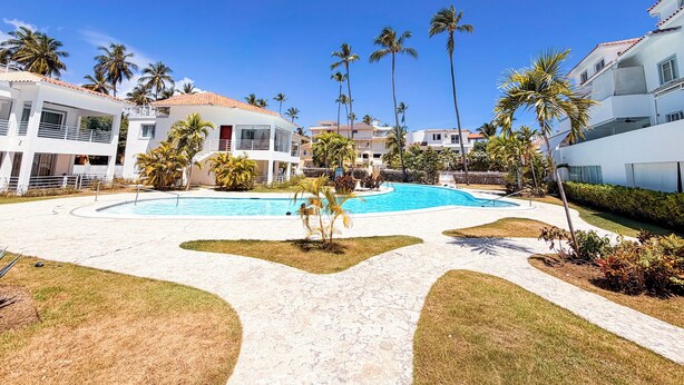 Ein Resort mit einem zentral gelegenen Pool, Palmen und modernen Gebäuden.
