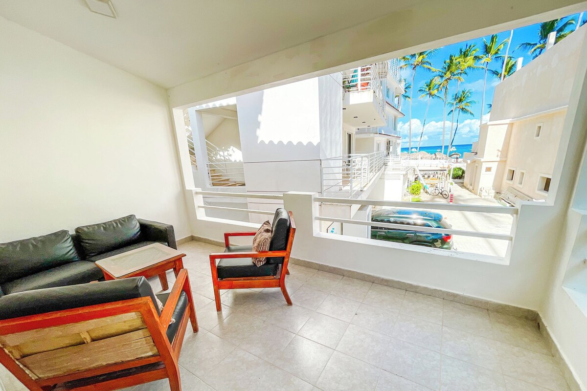 Varanda com vista para a praia e edifícios, mobiliada com um sofá e cadeiras.