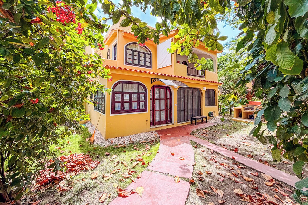 Uma casa de dois andares com porta vermelha, janelas grandes e uma varanda.