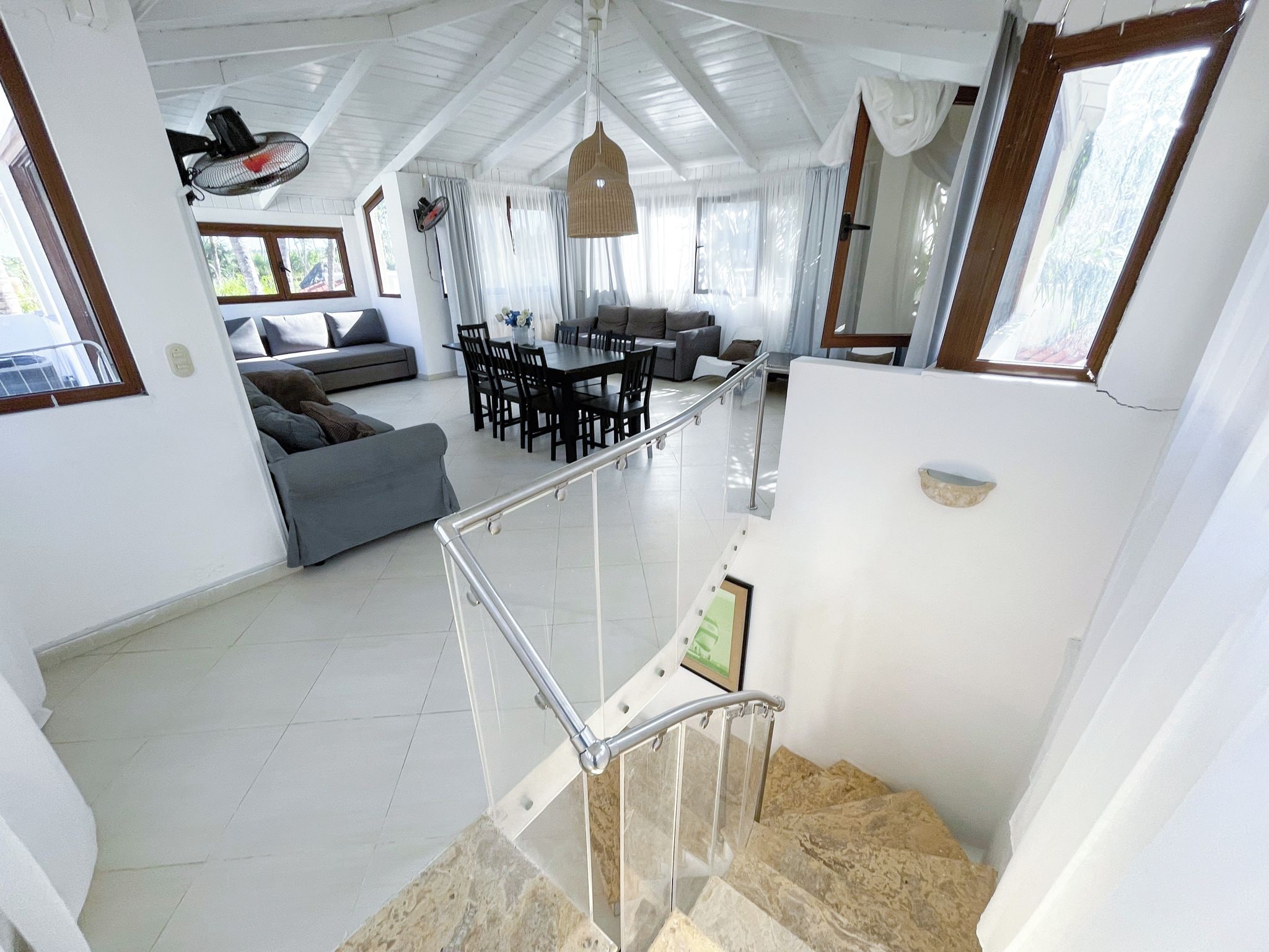 Ampla sala de estar com mesa e cadeiras, sofá e escada com guarda-corrimão de vidro.