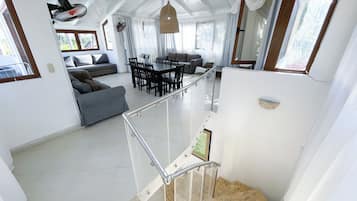 Ampla sala de estar com mesa e cadeiras, sofá e escada com guarda-corrimão de vidro.