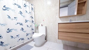 Ein Badezimmer mit Toilette, einer Duschkabine mit blauem Muster, einem Spiegel und einem Holzwaschtisch.