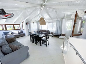 Uma sala de estar ampla com teto alto, uma mesa de jantar rodeada por cadeiras e um sofá.