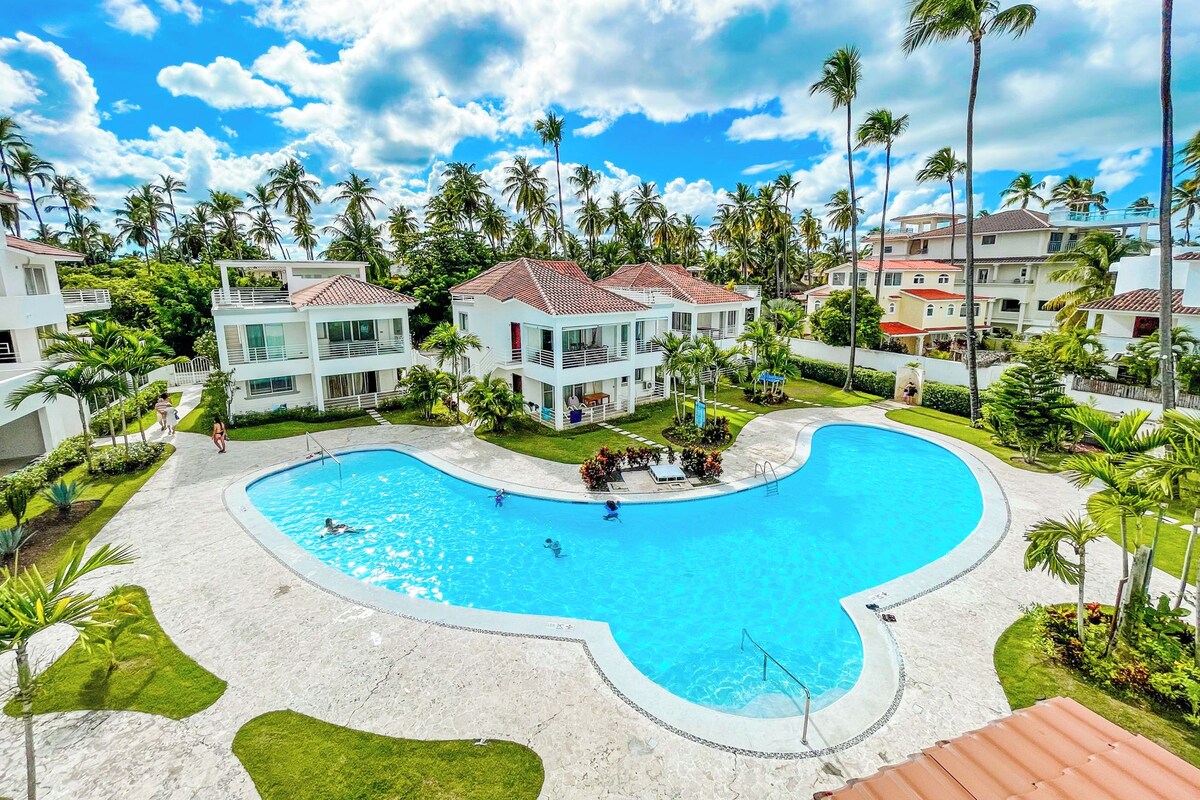 Um resort com uma piscina grande, edifícios de vários andares e palmeiras.