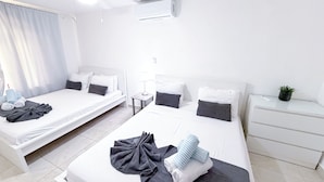 Ein Hotelzimmer mit zwei Betten, einem Deckenventilator, einer Klimaanlage, einem Nachttisch mit Lampe und einem kleinen Topfpflanzen.