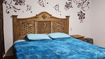 Un dormitorio con cabecera de madera, colcha azul y decoración mural.