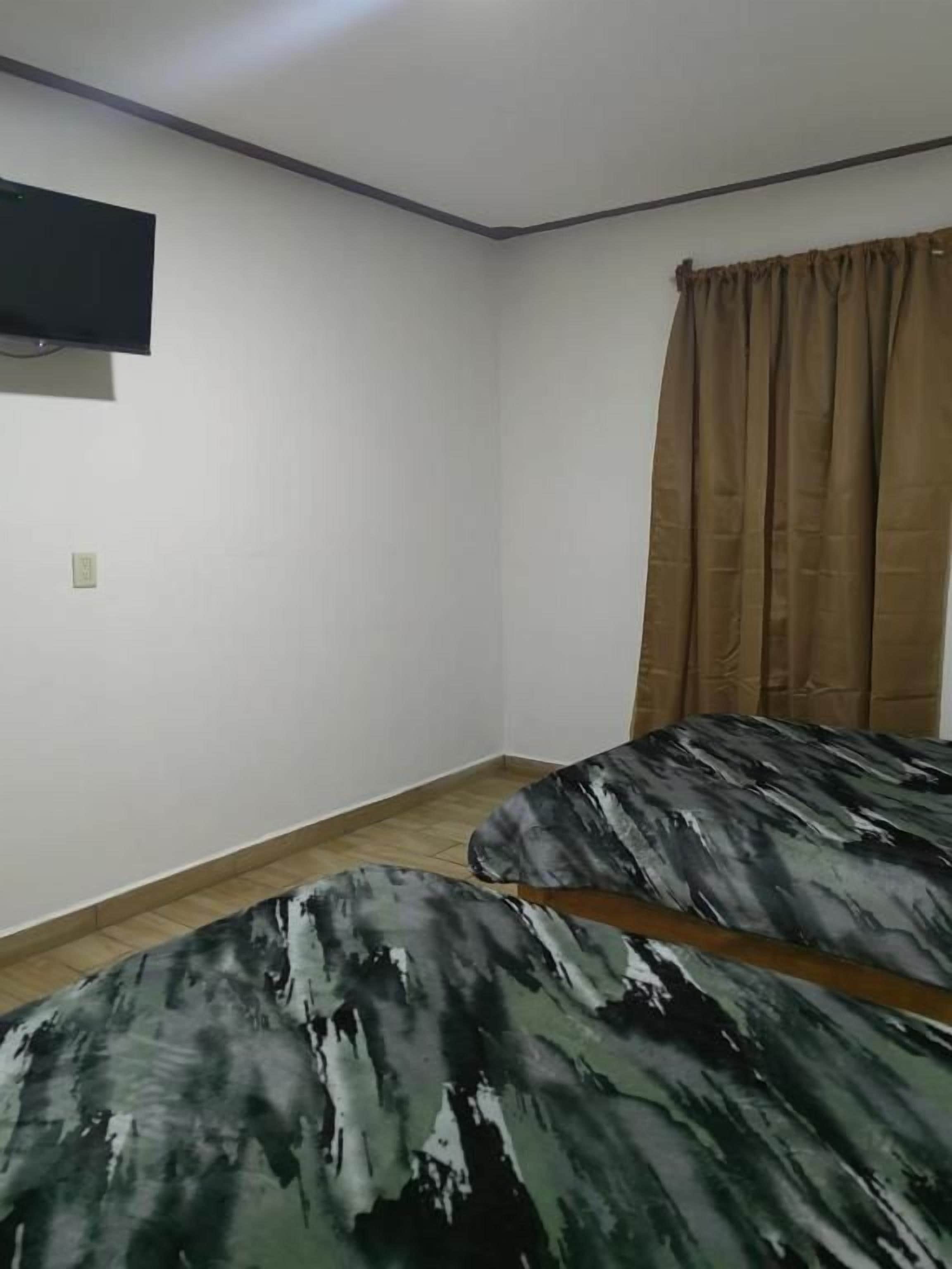 Una habitación con dos camas, un televisor de pantalla plana montado en la pared y una ventana con cortinas.