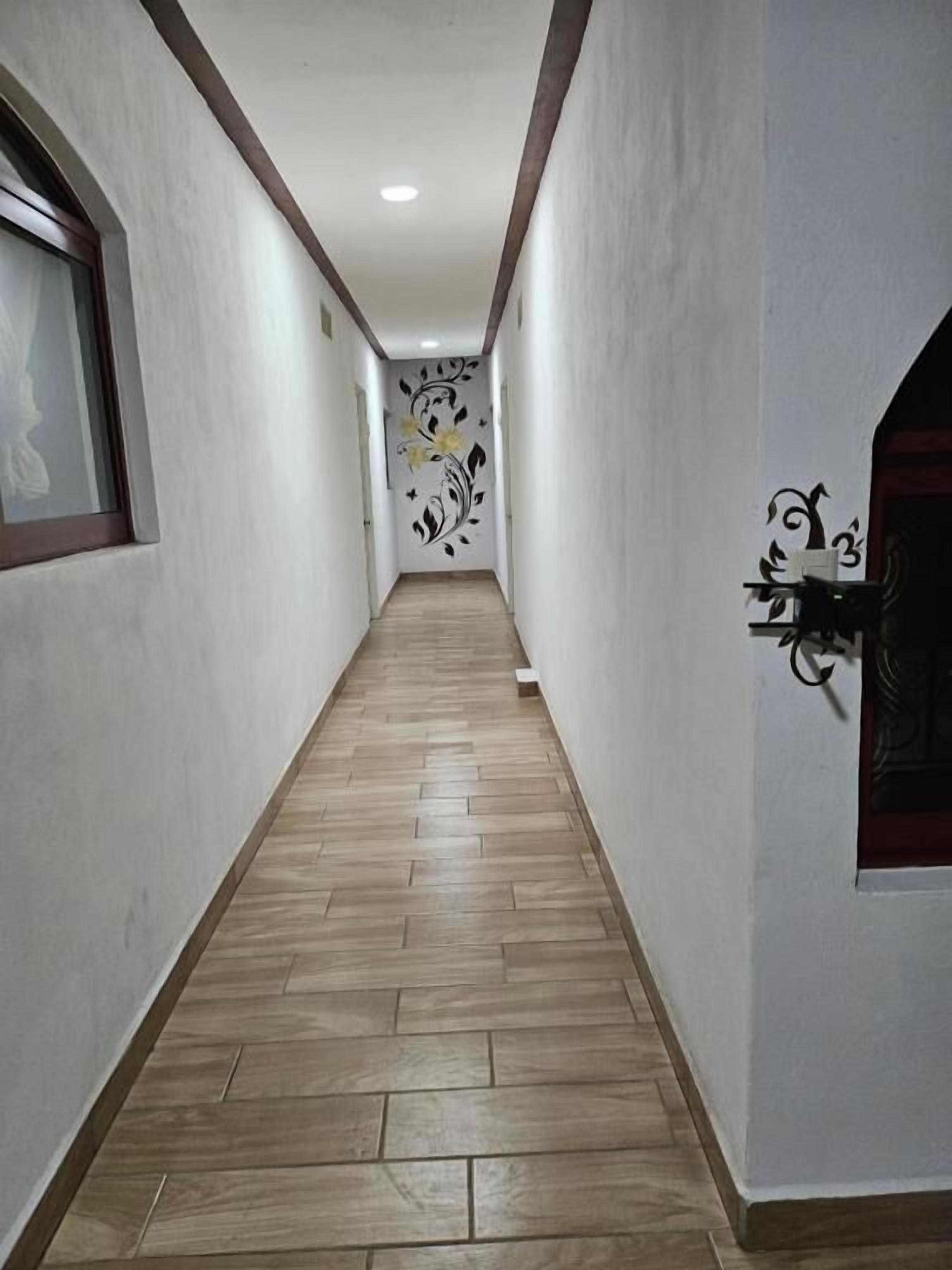 Un pasillo con piso de madera, paredes blancas y un adorno en la pared.