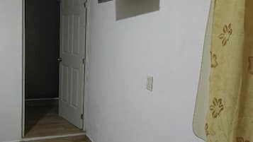 A room with a wooden floor, a closed door, a mounted flat-screen TV, and a curtain with a floral pattern.