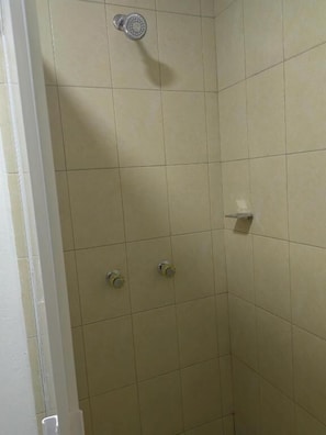 Un baño con azulejos color beige, un cabezal de ducha y dos grifos.