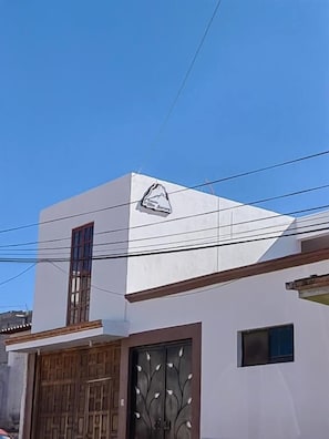 A white building with a mountain logo, a wooden door, and a small window. - Posada villa aurora (Ezequiel Montes)