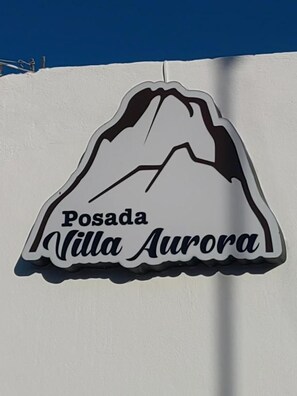 Un letrero con el contorno de una montaña y el texto 'Posada Villa Aurora'.