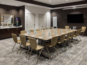 A conference room with a long table, chairs, water bottles, a whiteboard, and a television screen.