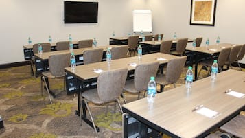 A conference room with tables, chairs, water bottles, a whiteboard, and a TV on the wall.