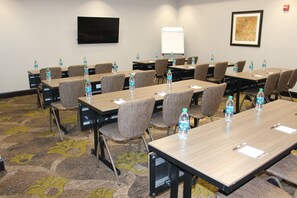 A conference room with tables, chairs, water bottles, a whiteboard, and a TV on the wall.