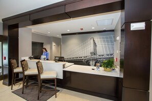 A hotel reception area with a modern design, featuring a reception desk, seating area, and a large wall mural of a bridge.