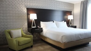 A hotel room with a large bed, two bedside lamps, a green armchair, and a patterned wall. - Roll-In Shower Studio | Free Breakfast + Pool (Miamisburg)