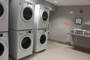 A laundry room with stacked front-loading washers and dryers, a fire extinguisher sign, and a notice about free guest laundry.