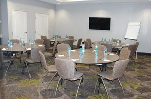 A conference room with round tables, chairs, water bottles, a whiteboard, and a TV on the wall.