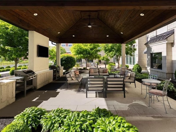 An outdoor patio with a grill, seating area, and a TV mounted on a wall.
