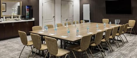 A conference room with a long table, chairs, water bottles, a whiteboard, and a TV screen.